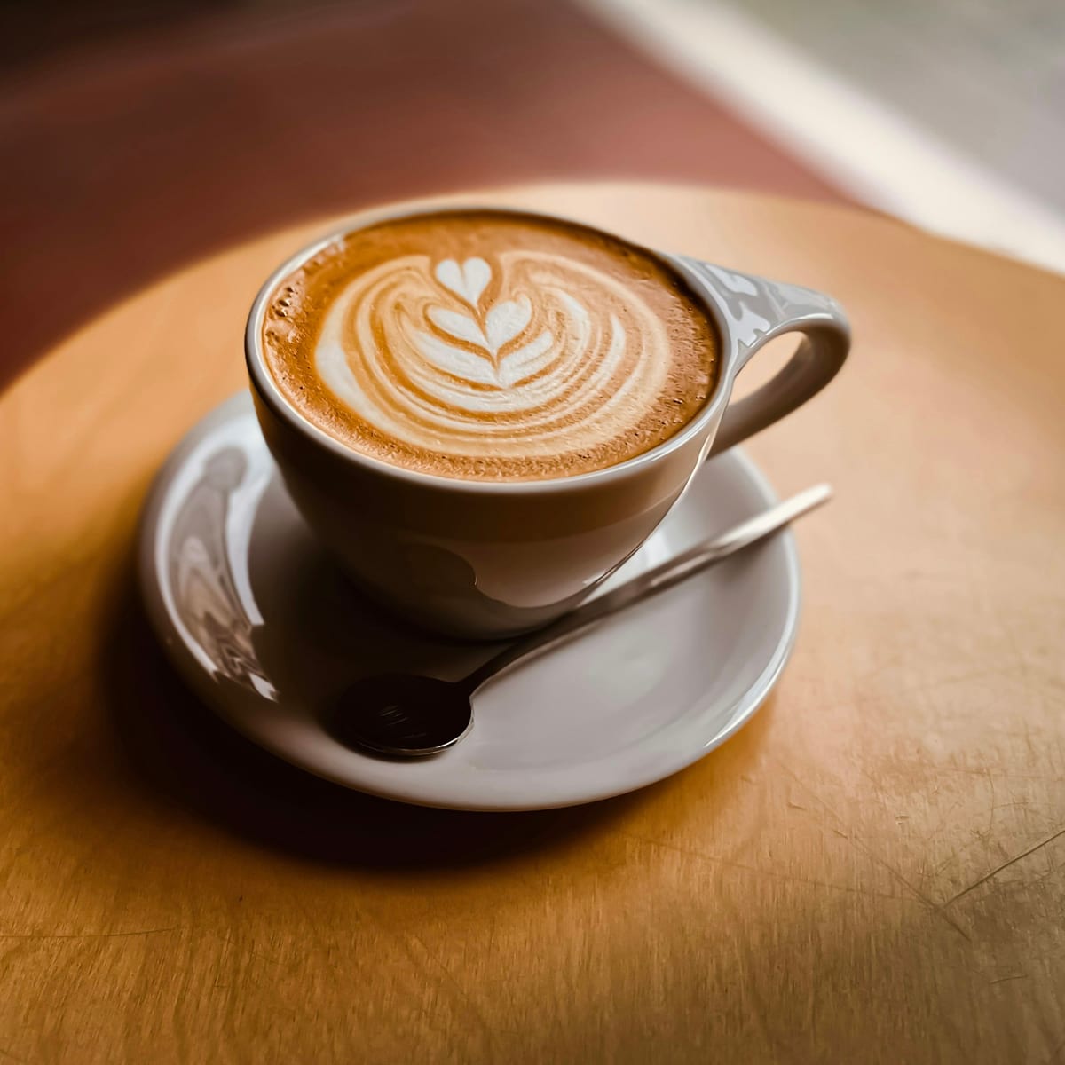 Milchkaffee mit Milchschaum-Muster auf einem runden Holztisch